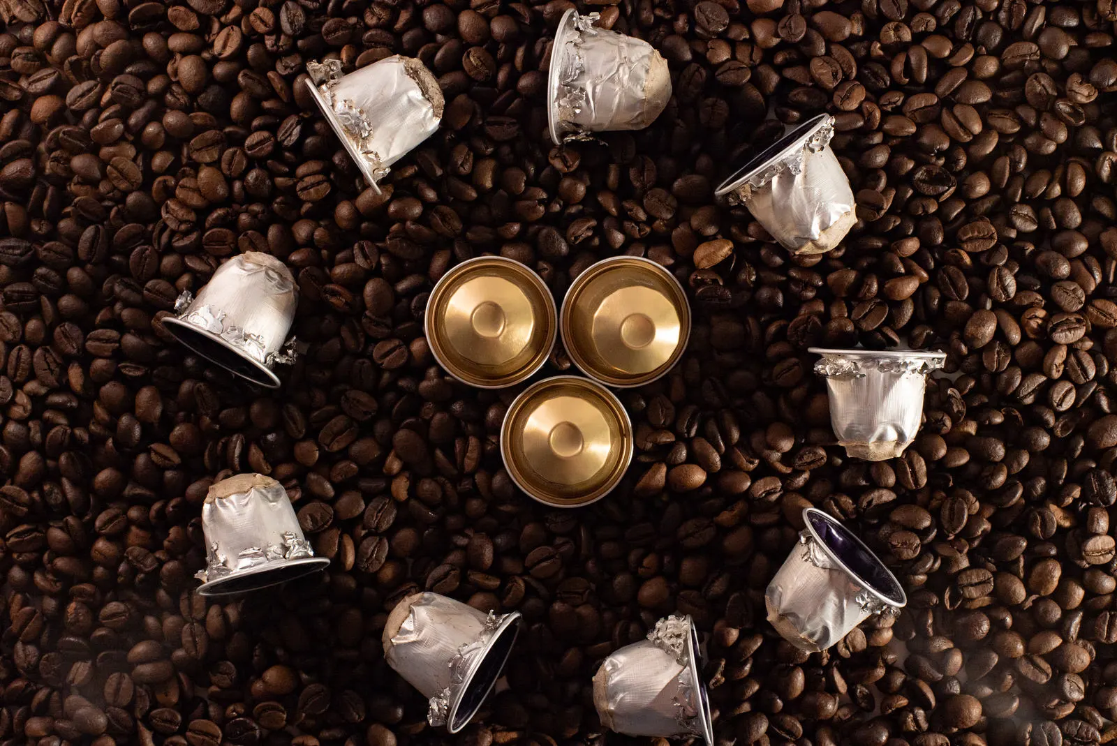 Capsule di caffè usate in alluminio sparse su chicchi di caffè
